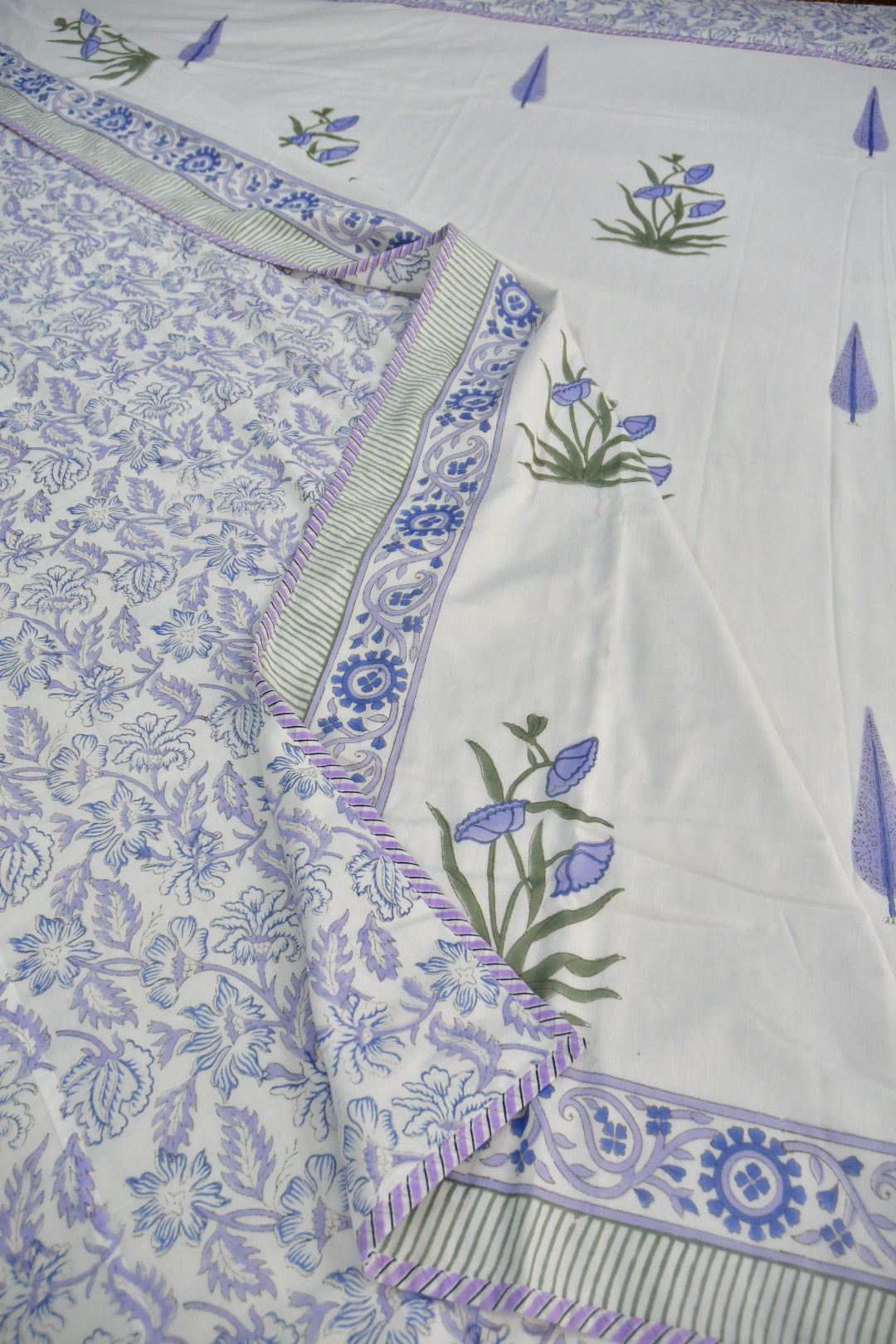 White cotton fabric with blue floral block print and embroidered motifs, featuring a decorative border and striped edge.