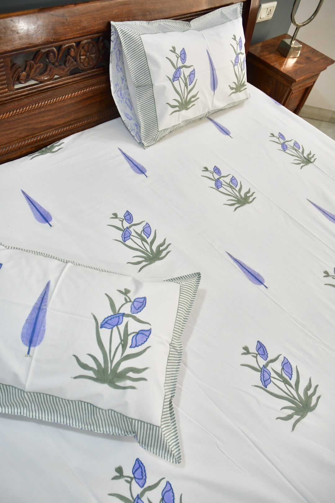 White cotton bed sheet set with a blue and green floral print, styled on a bed with matching pillowcases and a wooden headboard.