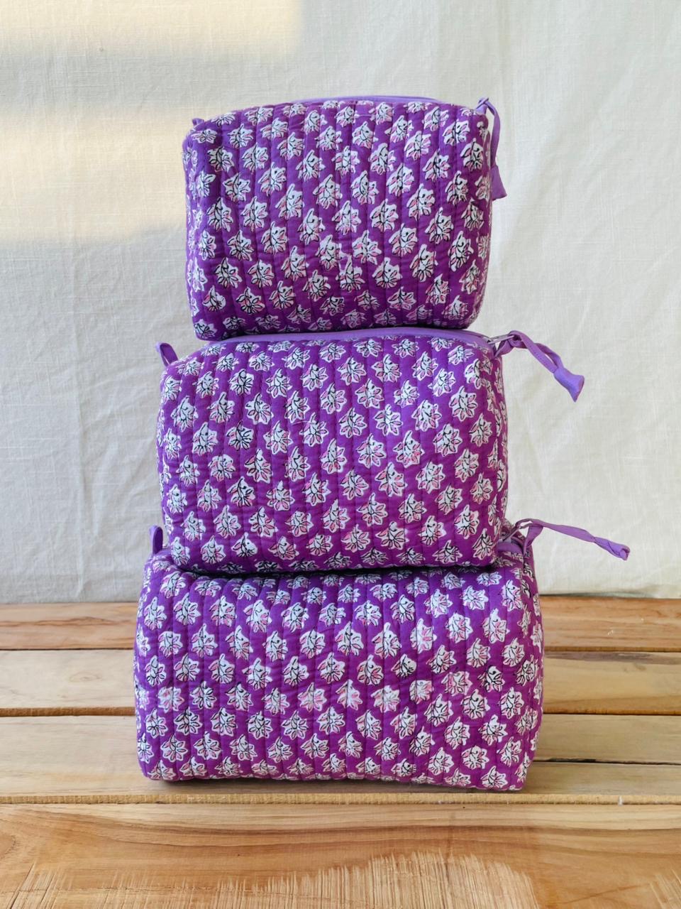 Three purple floral-patterned bags stacked on a wooden surface with a light gray background