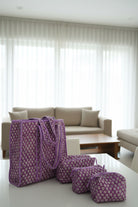 Purple patterned bags on a bed with floral bedding against a gray wall.