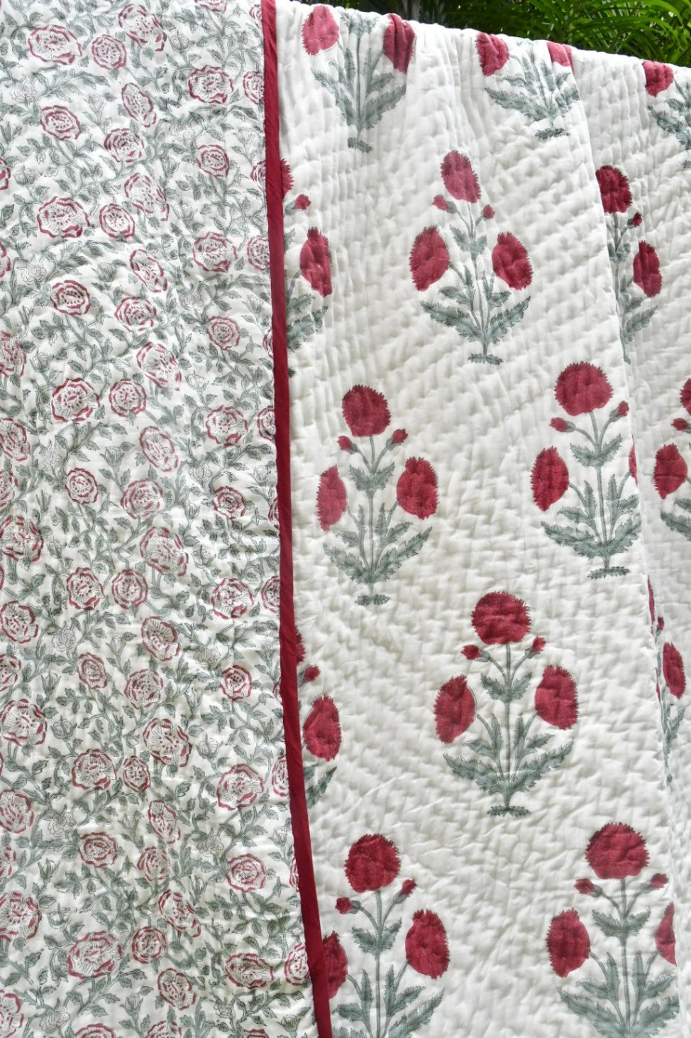 A close-up of a quilted textile with two floral patterns: one side shows small pink roses on a white background, and the other shows larger pink flowers with green stems on a white background, divided by a pink border.