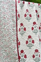 A close-up of a quilted textile with two floral patterns: one side shows small pink roses on a white background, and the other shows larger pink flowers with green stems on a white background, divided by a pink border.