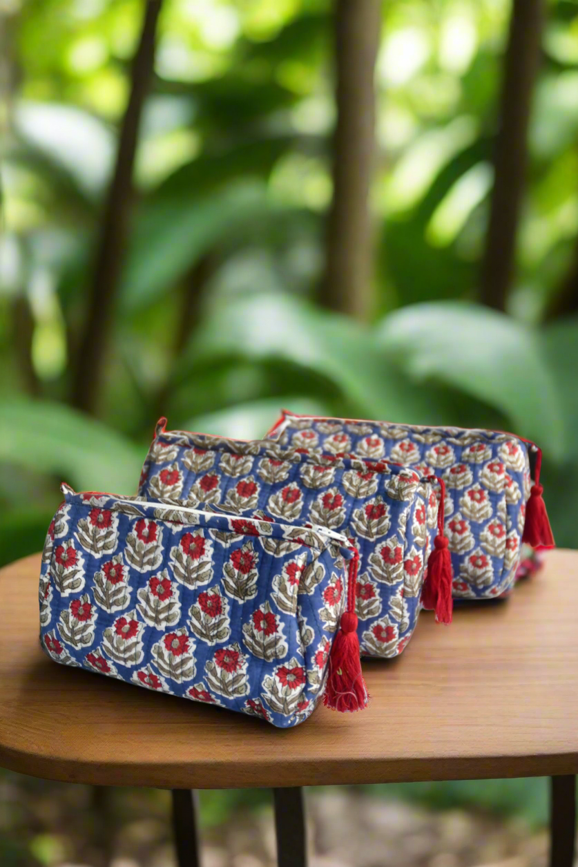 Two floral-patterned pouches with tassels on a wooden surface, blurred green foliage in the background