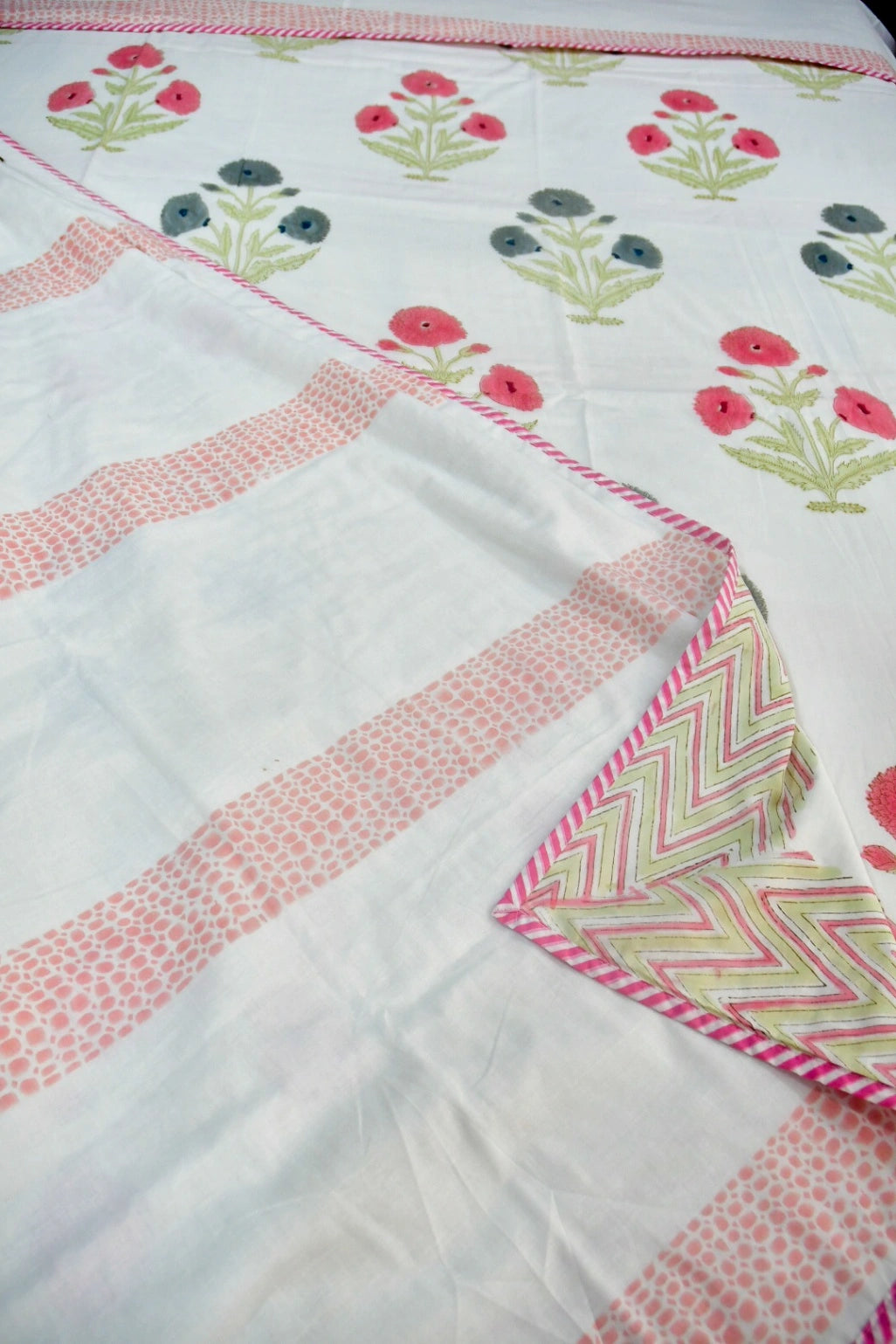 A close-up of a white fabric textile with pink patterned borders, pink and green floral motifs, and a folded corner showing a pink and green chevron pattern.