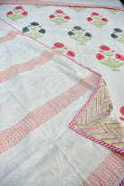 A close-up of a white fabric textile with pink patterned borders, pink and green floral motifs, and a folded corner showing a pink and green chevron pattern.