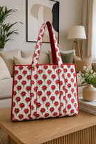 A quilted tote bag with a red rose pattern sits on a wooden coffee table in a cozy living room setting.