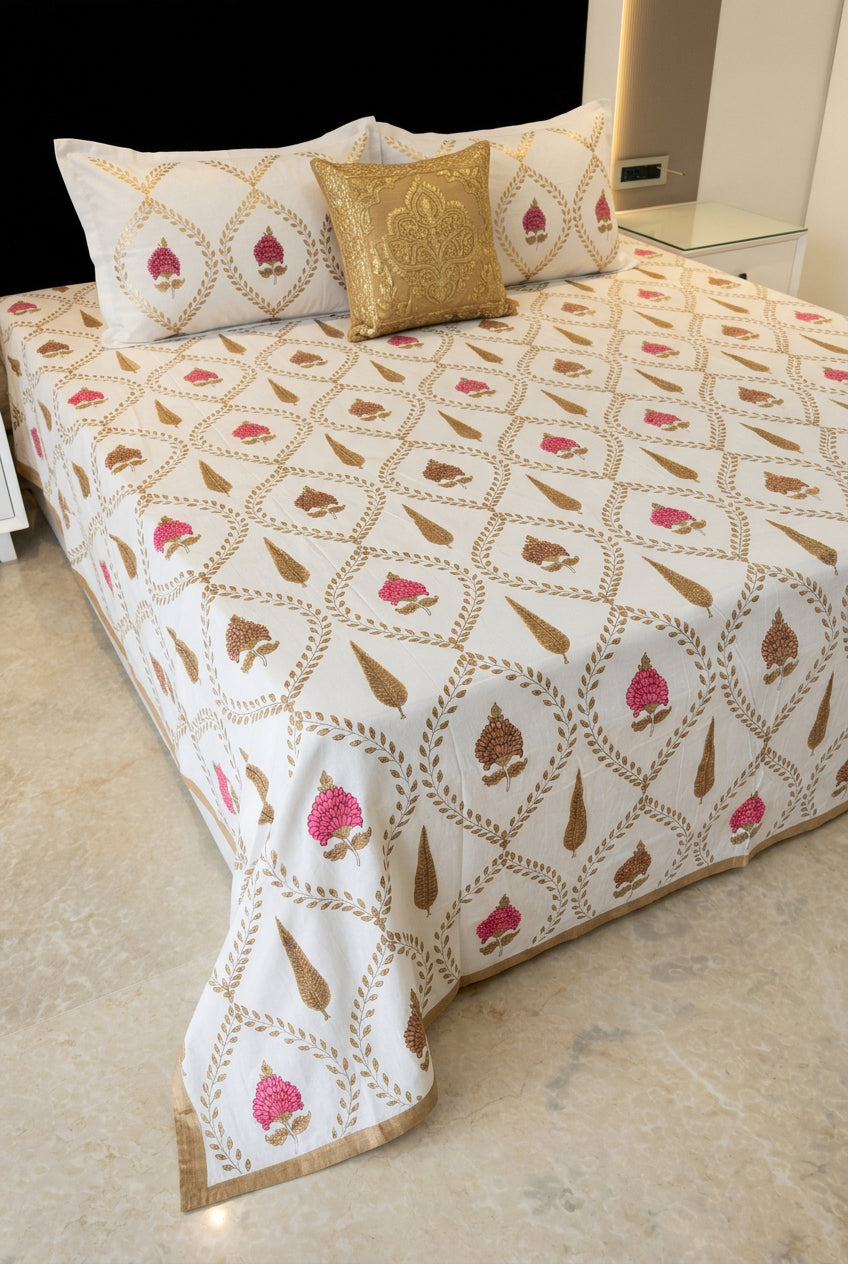 A bed dressed in a cream-colored cotton sheet with brown and pink block-printed motifs, styled with decorative pillows in a bedroom setting. The brand name ALBELI is visible as an overlay in the bottom-left corner.