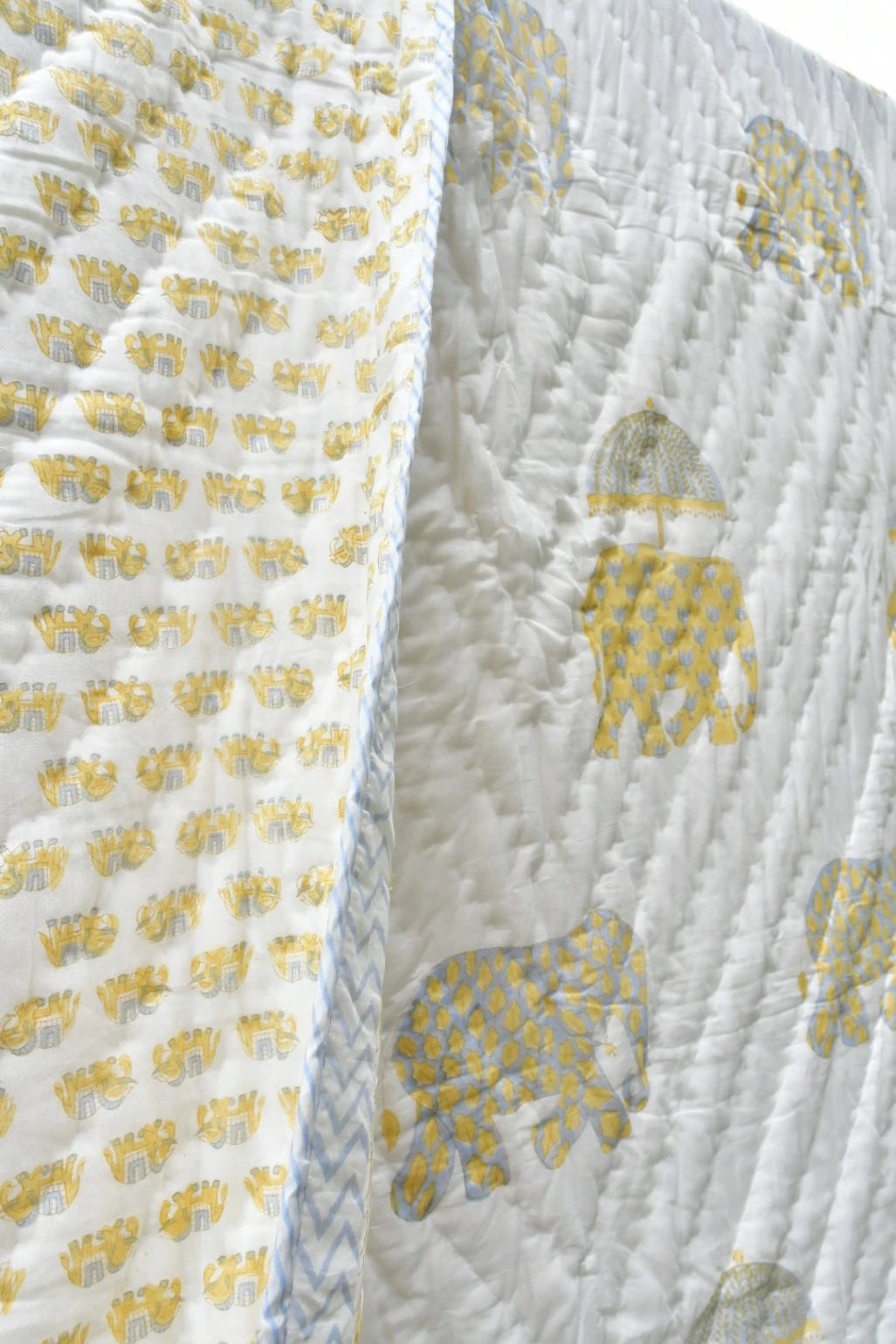 A close-up of a white quilted blanket featuring yellow elephant motifs and a blue-and-white chevron border.