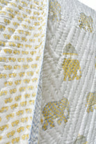 A close-up of a white quilted blanket featuring yellow elephant motifs and a blue-and-white chevron border.