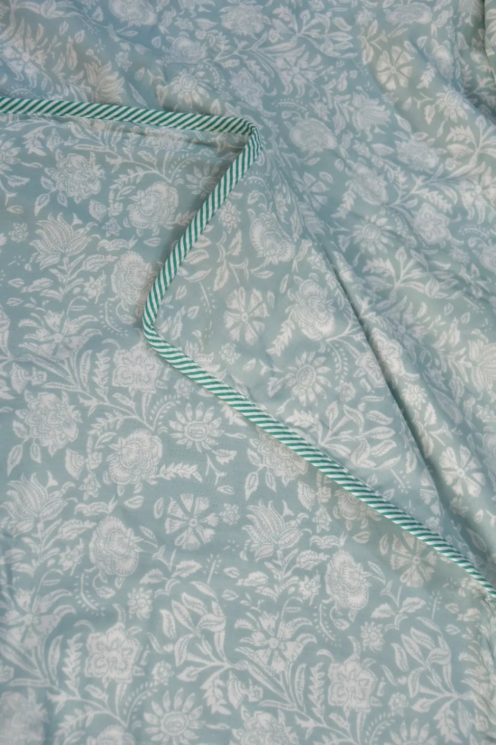 Floral patterned fabric with a striped green and white trim on a light blue background