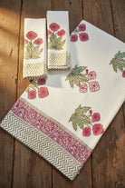 A set of white cotton kitchen towels with pink floral prints and green leaves, featuring decorative borders, displayed on a rustic wooden background.