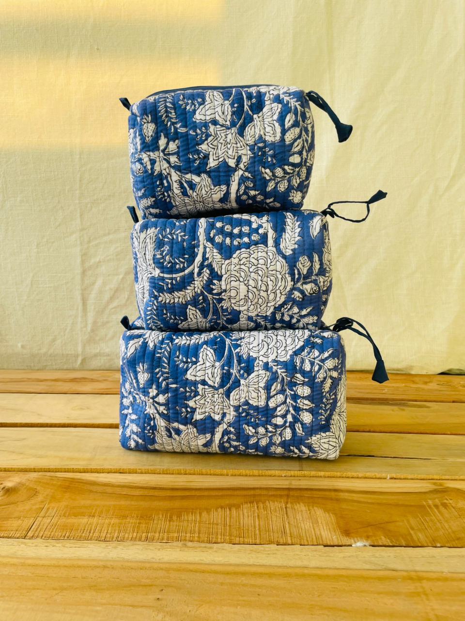 Stack of blue floral-patterned pouches on a wooden surface with a beige background