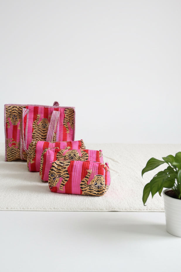 Three pink and gold patterned pouches on a white surface with a plant in the background.