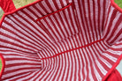 Close-up of the interior of a red and white striped fabric tote bag, showing stitched lining and a top pocket, photographed outdoors on grass.