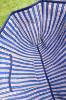 Close-up of the inside of a striped blue and white fabric umbrella, showing the stitched canopy lining and a small pocket, with green grass visible in the background.