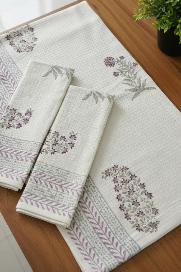 Set of embroidered towels on a wooden surface with a plant in the background