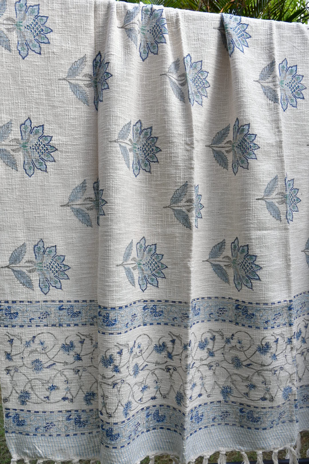 White throw with blue floral patterns, folded and displayed outdoors.