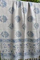 White throw with blue floral patterns, folded and displayed outdoors.
