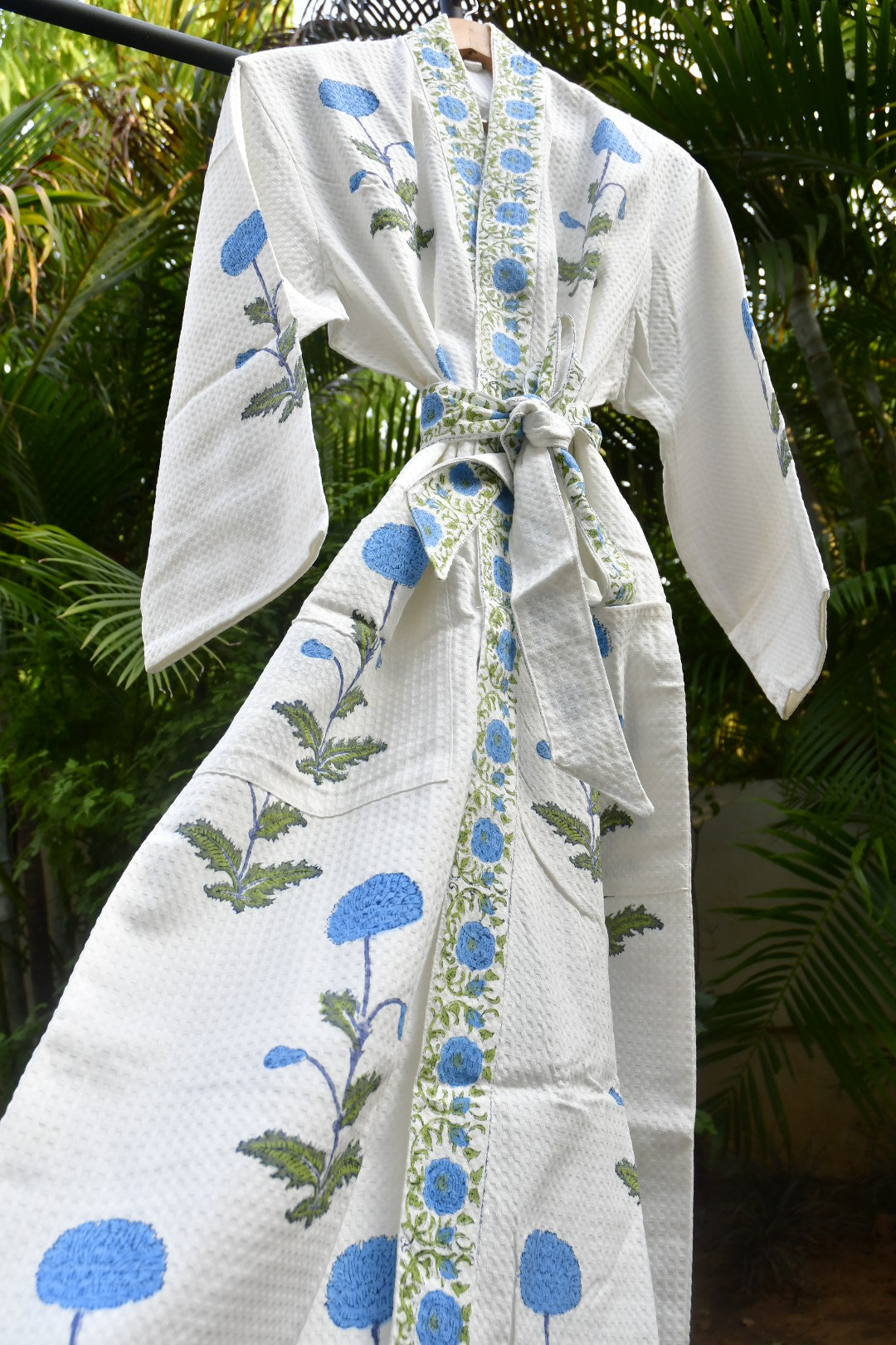 White fabric with blue floral patterns draped over a green leafy background
