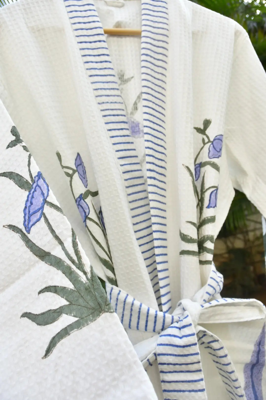 White & purple bathrobe with blue floral embroidery on a mannequin against a blurred green background