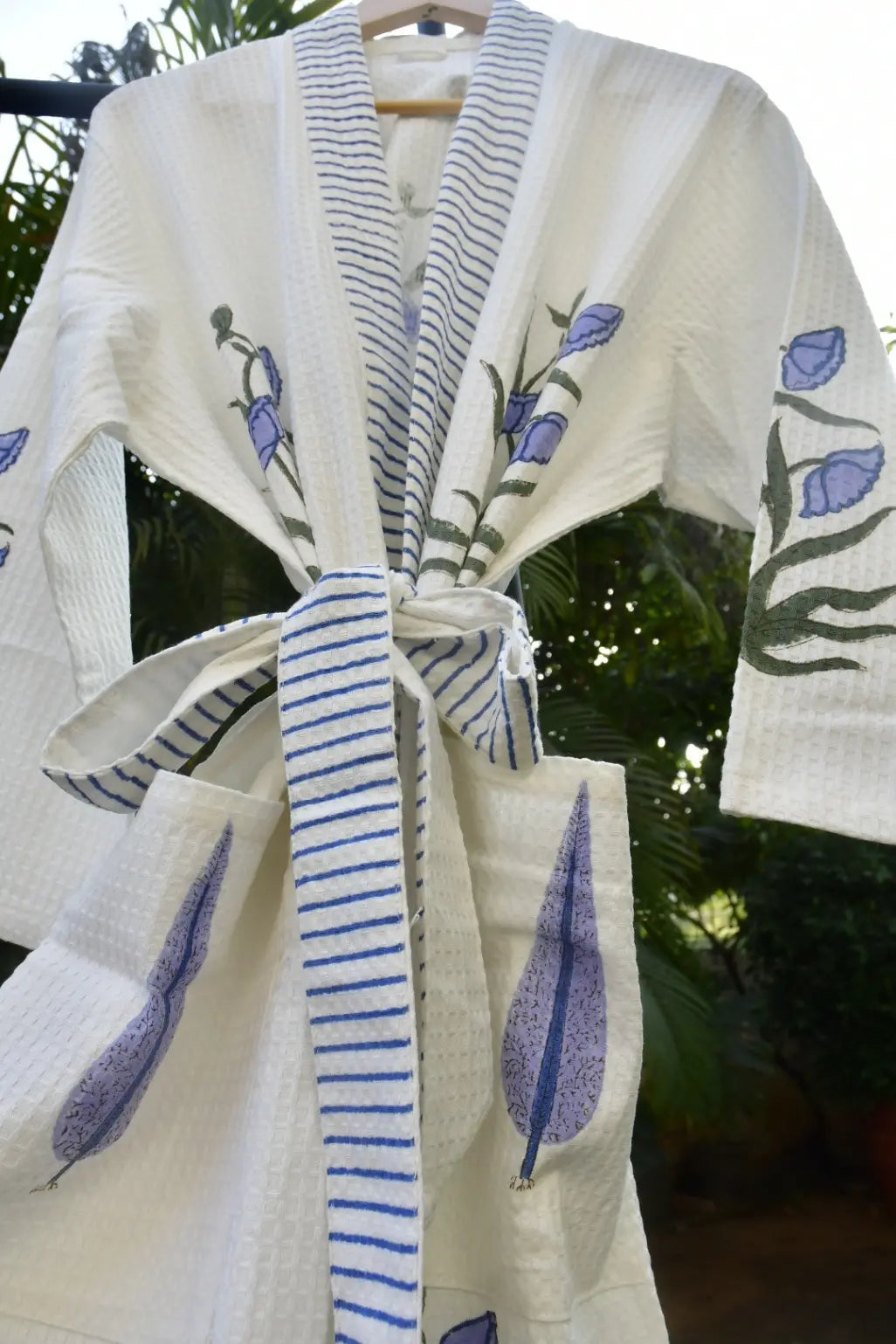 White robe with blue floral patterns on a hanger against a blurred green background