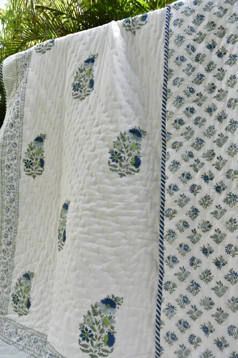 White quilt with blue floral patterns hanging outdoors