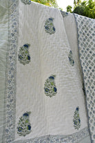 White quilt with blue floral patterns draped over a white surface outdoors.