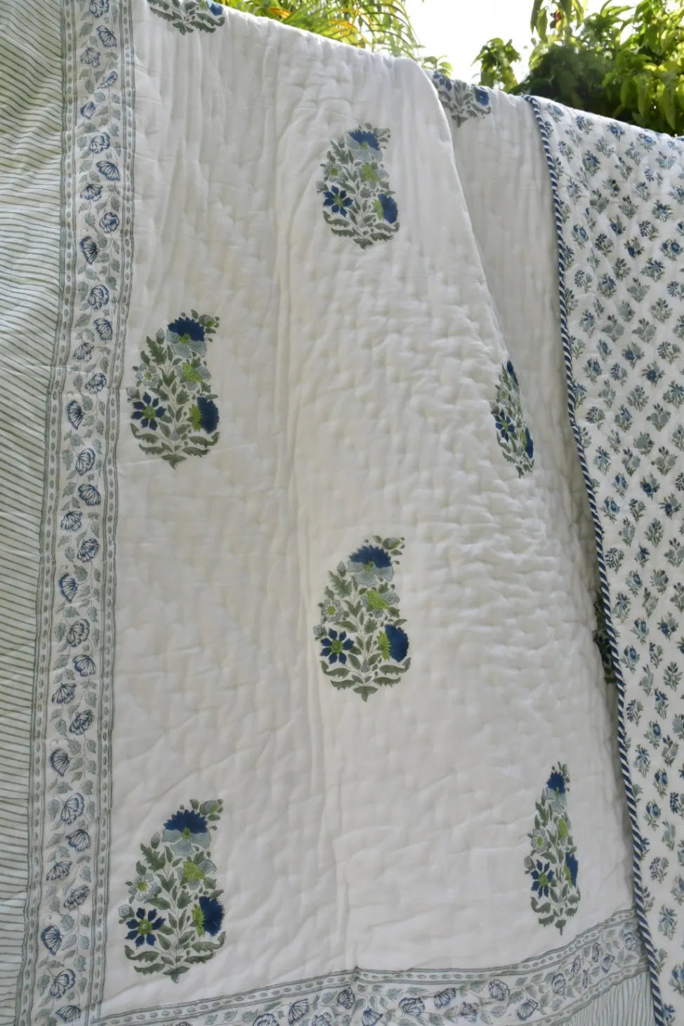 White quilt with blue floral patterns draped over a white surface outdoors.