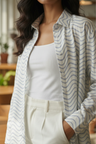 Person wearing a light-colored striped shirt over a white top and pants, standing indoors.