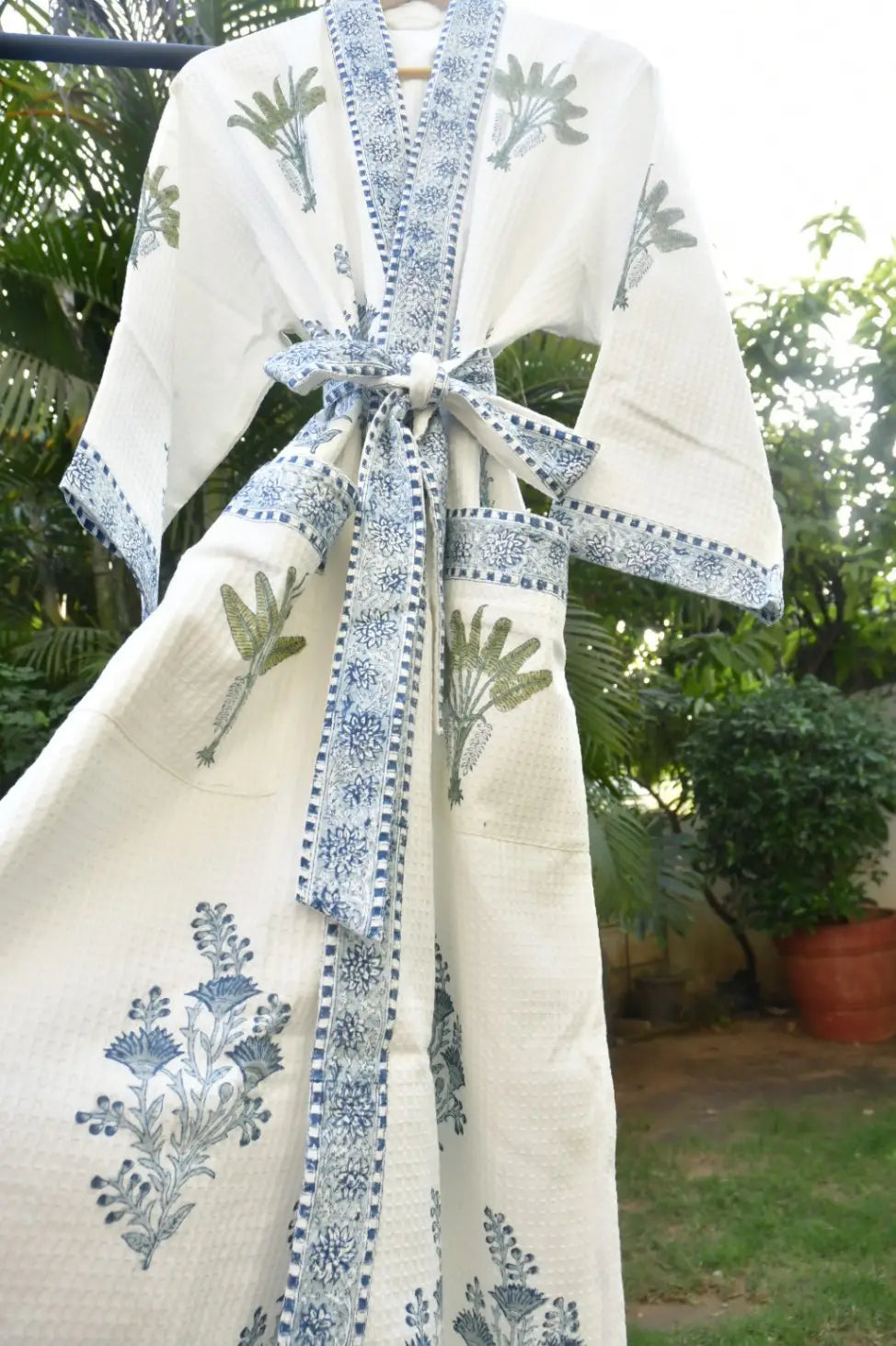 White garment with blue floral embroidery and a large bow, hanging outdoors.