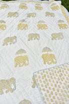 A white quilted blanket featuring a repeating pattern of elephants carrying yellow umbrellas, with a folded corner showing a light blue and white patterned reverse side.