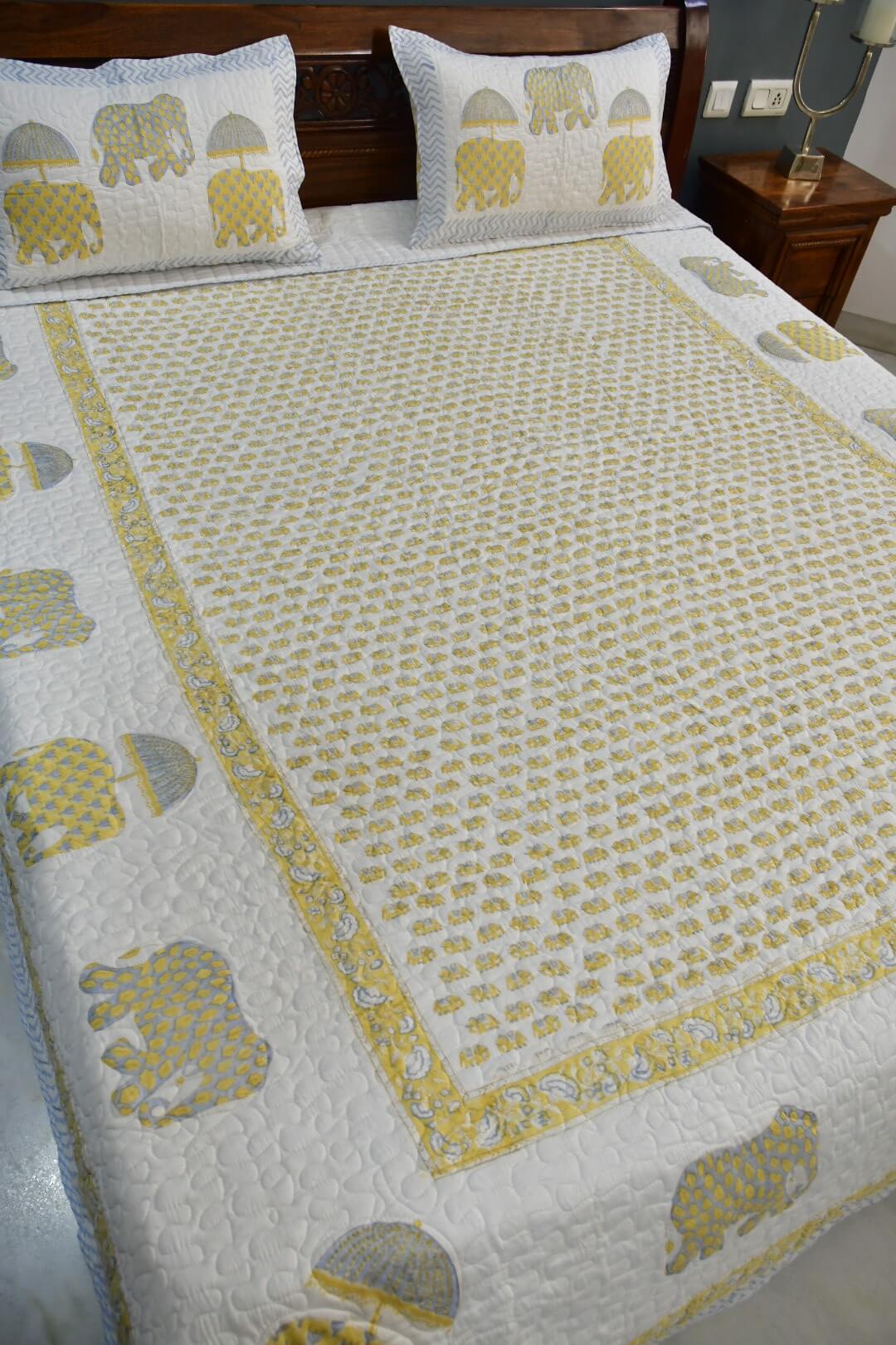 A quilted bedspread and matching pillowcases featuring a white background with a yellow elephant pattern and border, styled on a bed in a bedroom setting.
