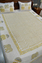 A quilted bedspread and matching pillowcases featuring a white background with a yellow elephant pattern and border, styled on a bed in a bedroom setting.