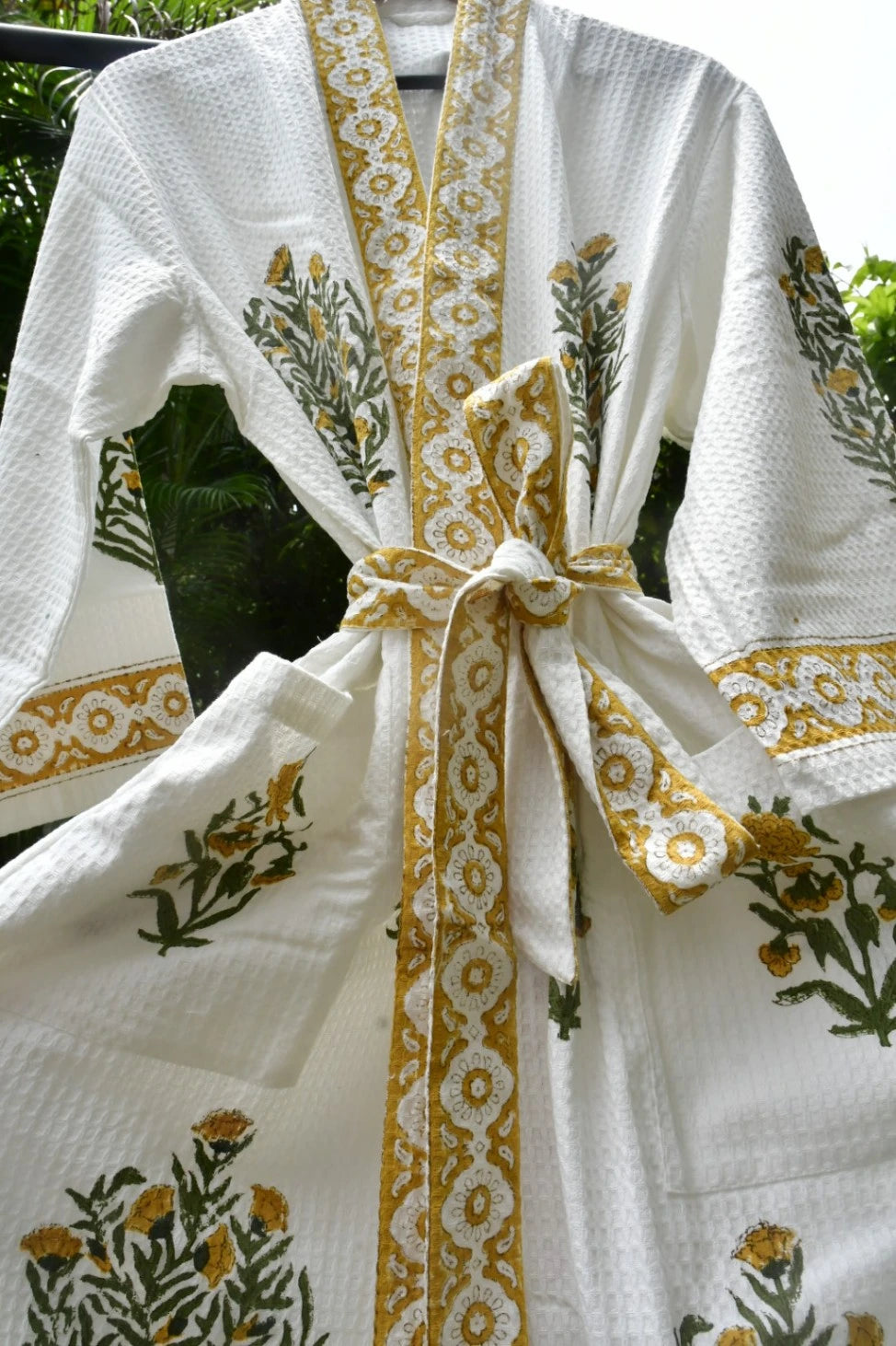 A white textured cotton robe with yellow and green floral embroidery, featuring a matching tie belt and a decorative yellow border along the collar and front opening.