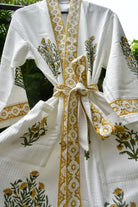 A white textured cotton robe with yellow and green floral embroidery, featuring a matching tie belt and a decorative yellow border along the collar and front opening.
