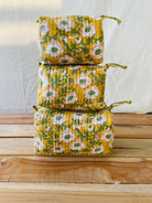 Stack of yellow floral fabric bags on a wooden surface with a white background