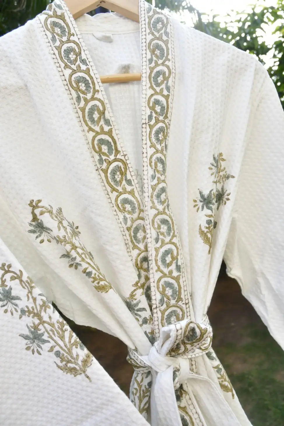 White garment with green floral embroidery on a wooden hanger against a blurred natural background