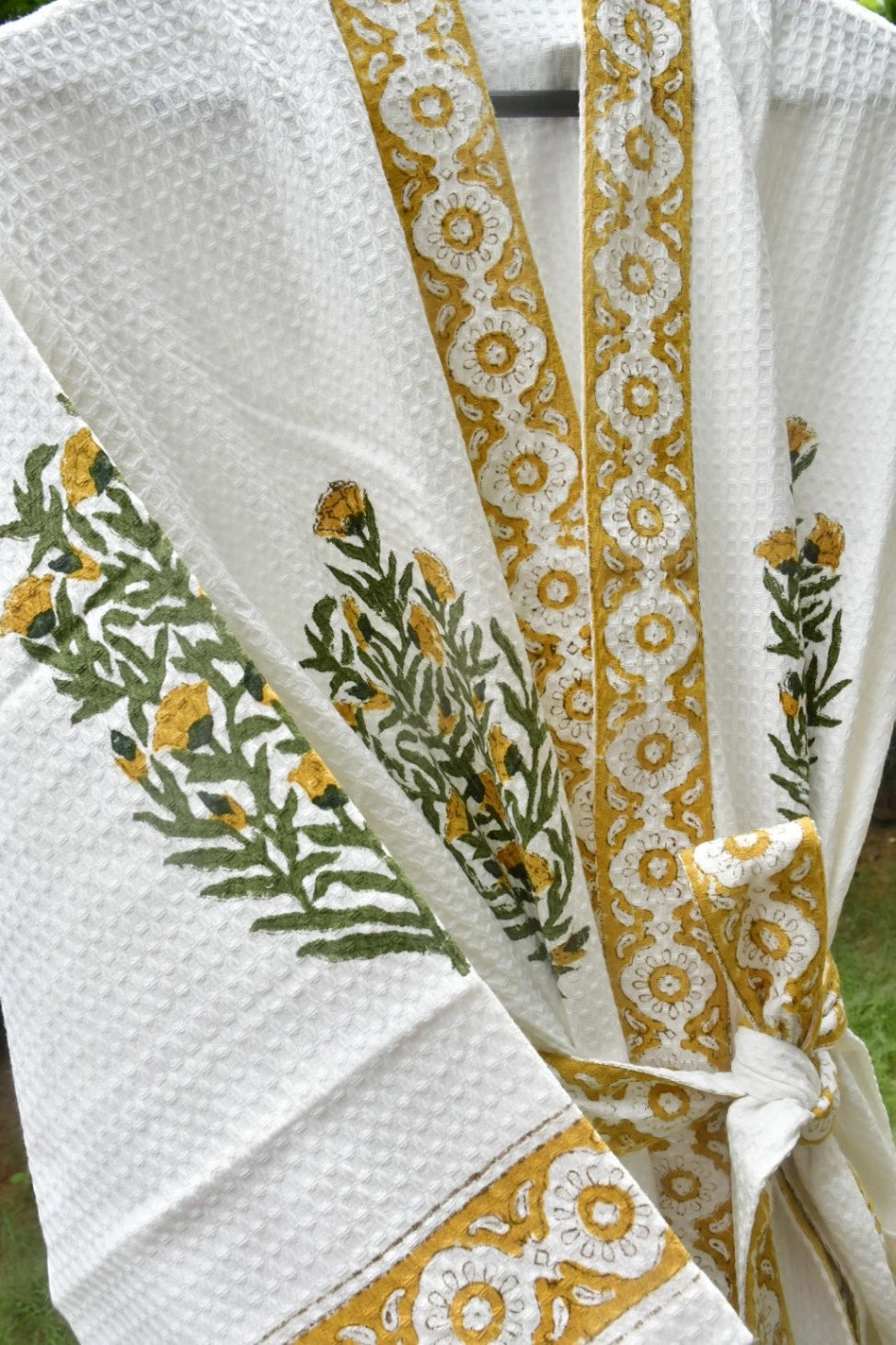 White textured waffle-knit robe with mustard yellow floral border trim and green/yellow embroidered botanical motifs, tied at the waist.