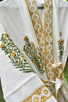 White textured waffle-knit robe with mustard yellow floral border trim and green/yellow embroidered botanical motifs, tied at the waist.