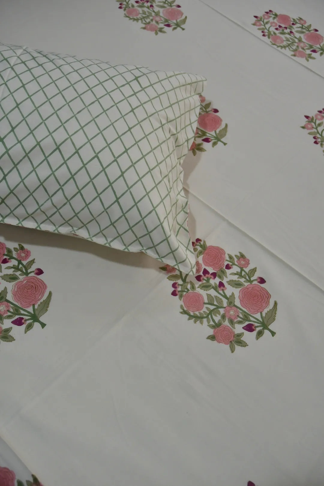 Floral patterned bedsheet with a green checkered pillow on a white background