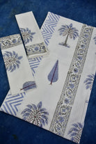 A set of white cotton towel set with blue and gray block-printed palm tree and floral motifs, laid flat on a dark blue textured background.