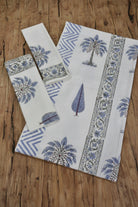A set of white cotton towels, including a large rectangular cloth and two smaller square pieces, printed with blue palm tree motifs, floral borders, and geometric patterns, arranged on a rustic wooden surface.