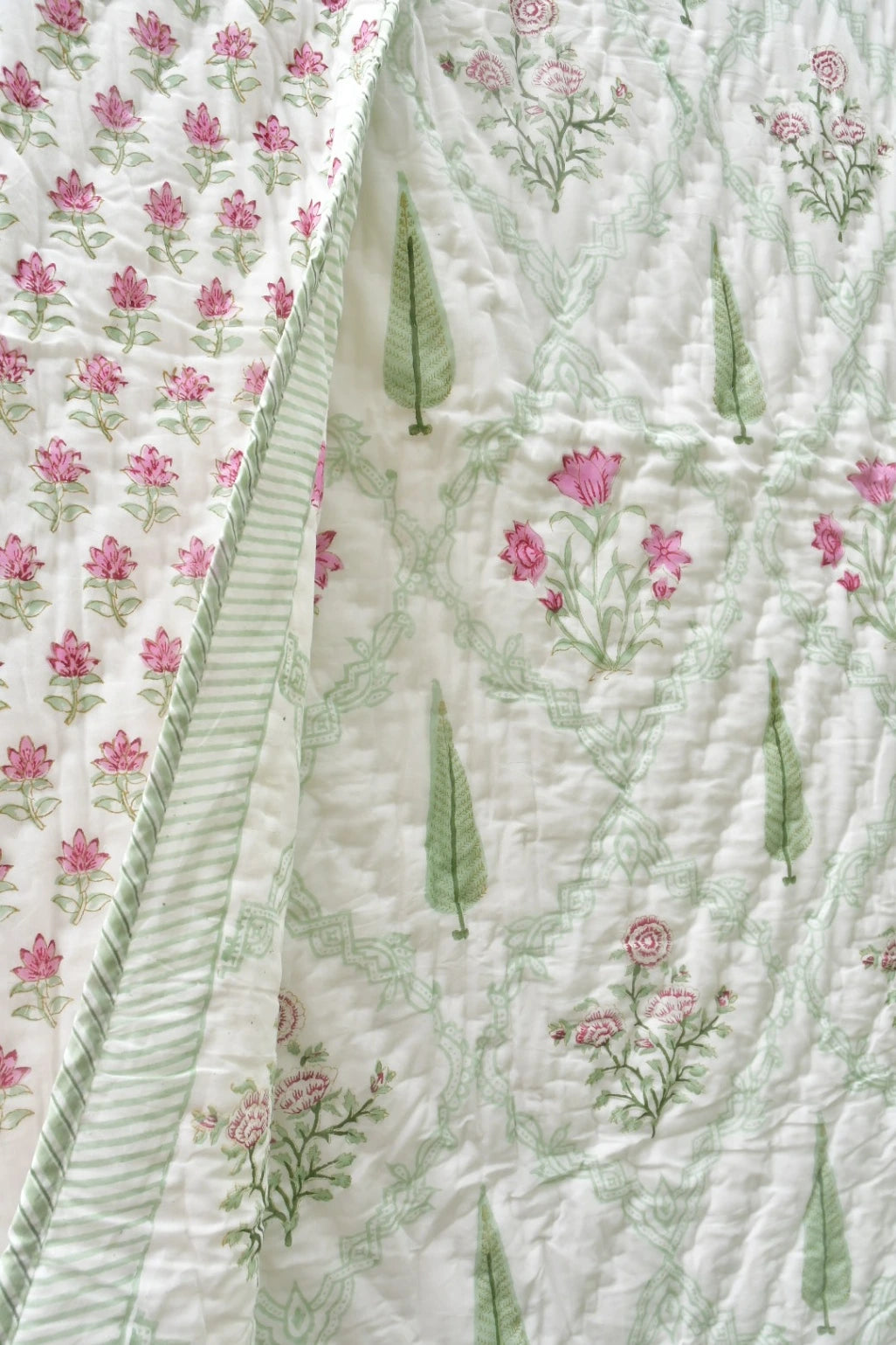 A close-up of a quilted fabric with a white background, featuring pink floral prints, green leaf motifs, and a striped border.