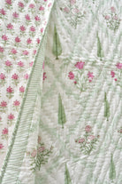 A close-up of a quilted fabric with a white background, featuring pink floral prints, green leaf motifs, and a striped border.