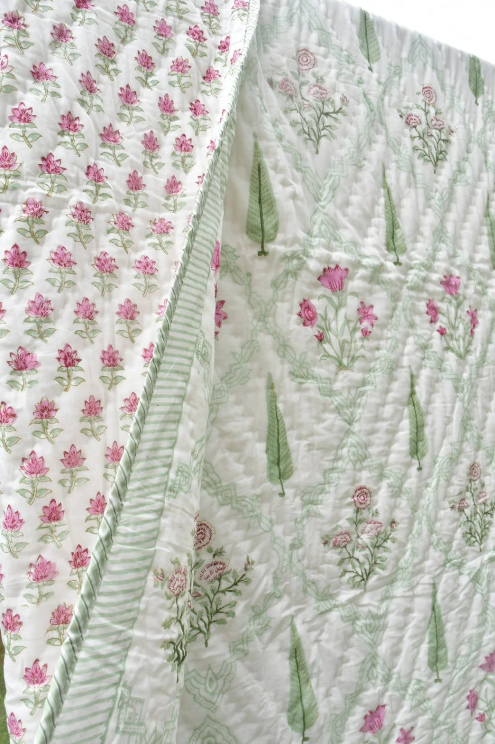 A close-up of a quilted fabric panel with a white background, featuring pink floral prints, green leaf motifs, and a striped border.
