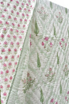 A close-up of a quilted fabric panel with a white background, featuring pink floral prints, green leaf motifs, and a striped border.
