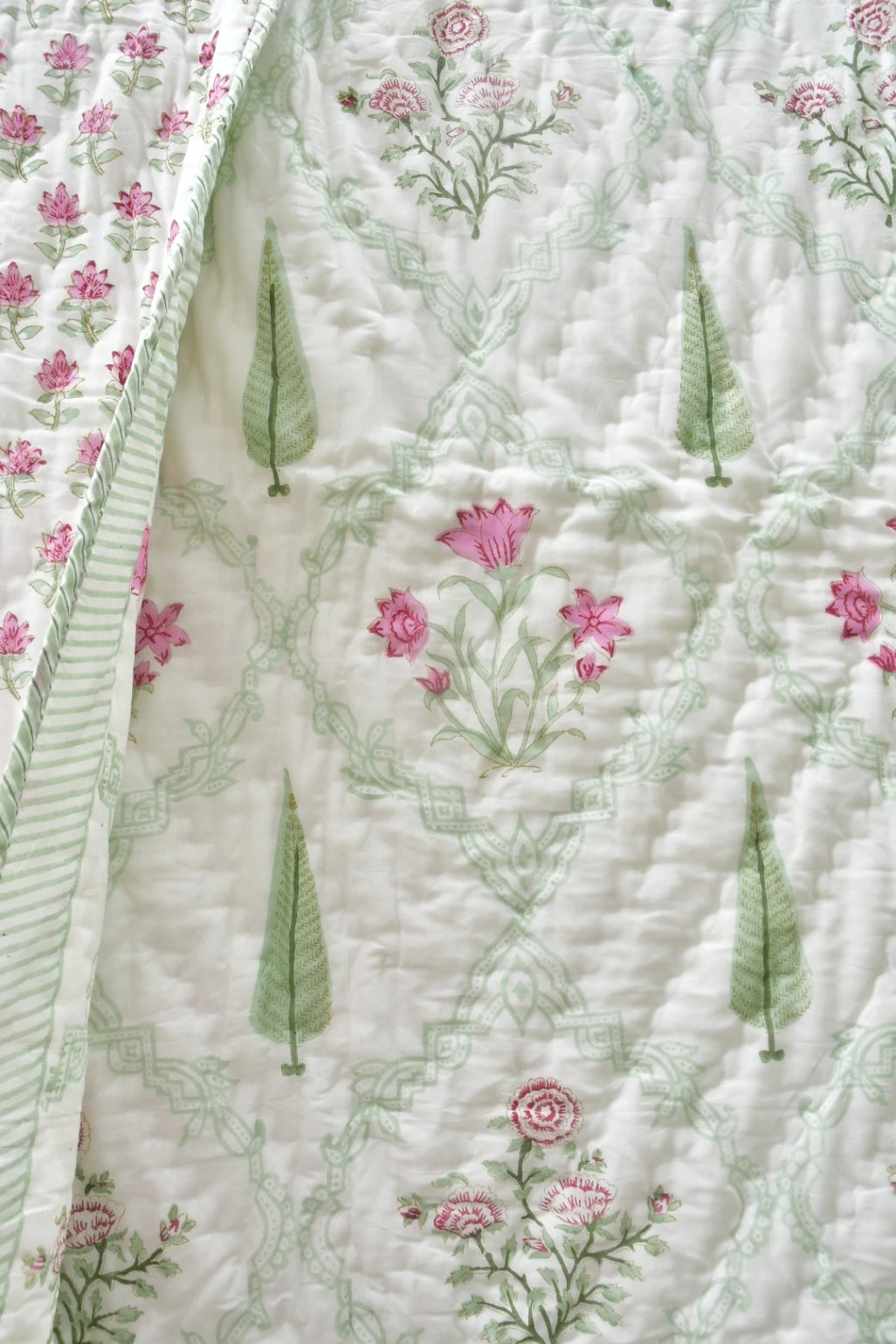 A close-up of a quilted fabric featuring a delicate pattern of pink flowers, green leaves, and a light green damask lattice design on an off-white background.