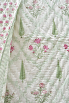 A close-up of a quilted fabric featuring a delicate pattern of pink flowers, green leaves, and a light green damask lattice design on an off-white background.