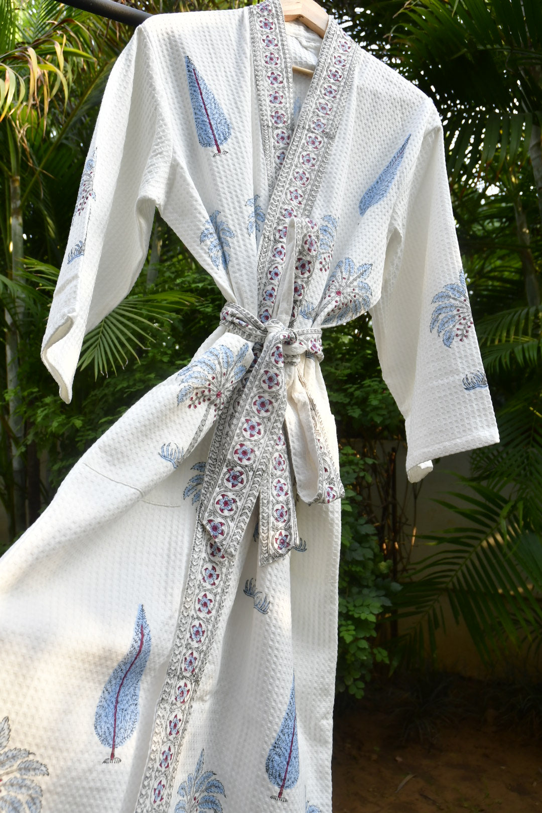 White robe with blue bird pattern and decorative ribbon against a blurred green background